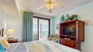 Hotellihuone, jossa on sänky, televisio puukehikossa, kattotuuletin, ikkuna verhoilla ja näkymä ulos.
