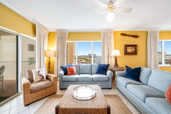 A living room with a sofa, two armchairs, a coffee table, and a ceiling fan. - Beachfront condo with Gulf front shared pool, private balcony, and grilling area (Orange Beach)