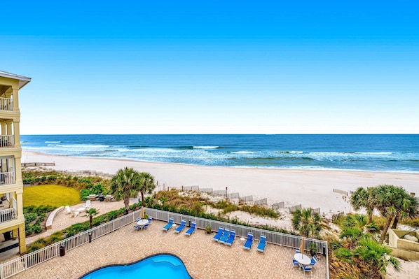 A pool area with lounge chairs and a view of the ocean. - Beachfront condo with Gulf front shared pool, private balcony, and grilling area (Orange Beach)