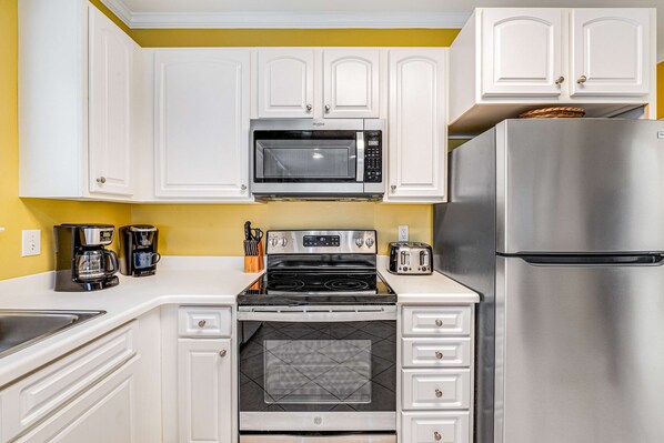 A kitchen with white cabinets, a stainless steel refrigerator, a microwave, a stove, and a toaster. - Beachfront condo with Gulf front shared pool, private balcony, and grilling area (Orange Beach)