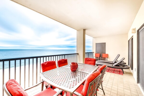 A balcony with a table and chairs, a view of the sea, and a door to the right. - Beachfront condo with shared outdoor pool, heated indoor pool, sauna, & grill area (Orange Beach)