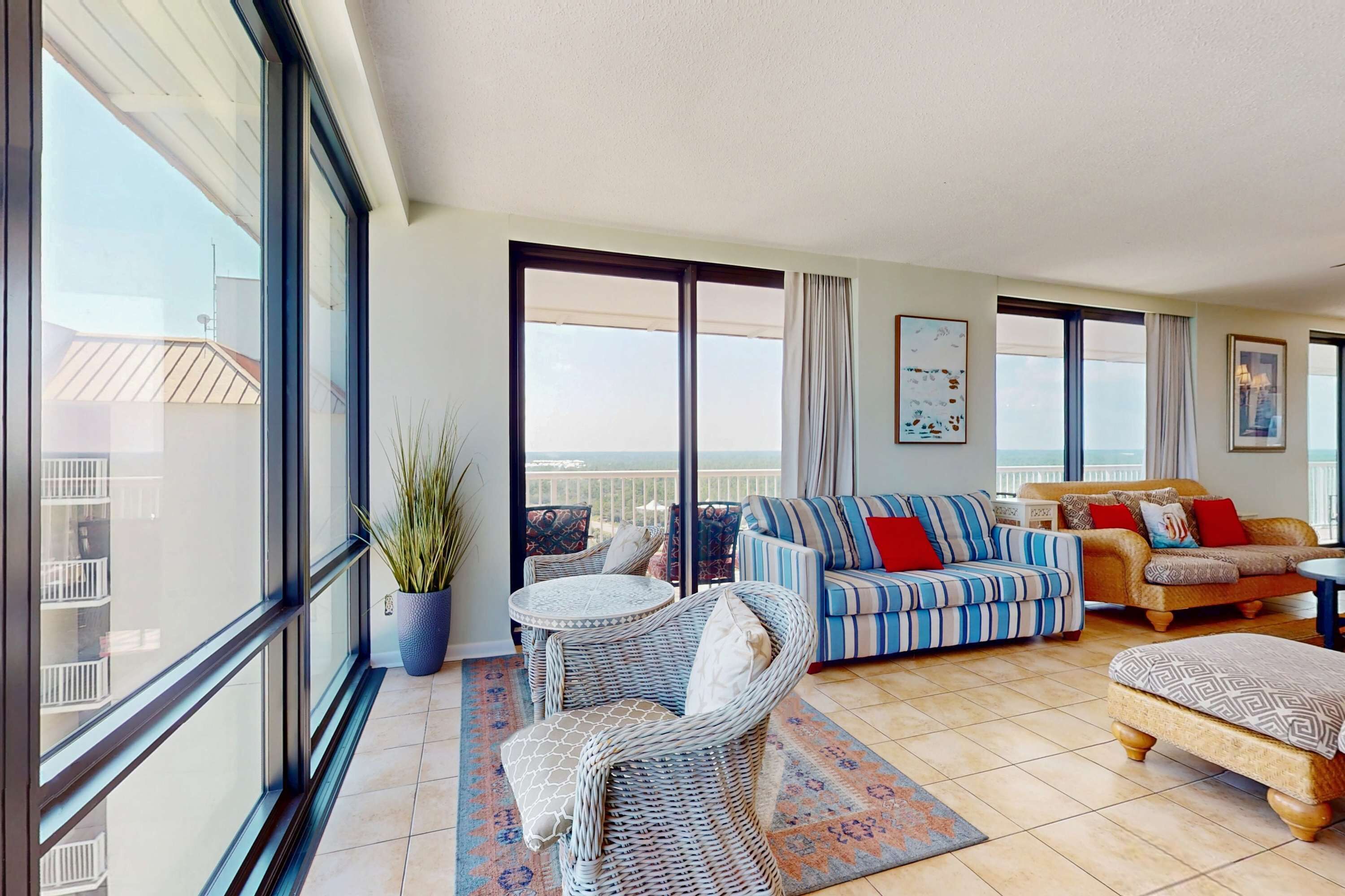 A spacious balcony with a view, wicker furniture, a striped sofa, and a patterned rug.
