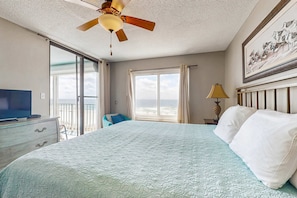A hotel room with a bed, a ceiling fan, a television, a window with curtains, and a painting on the wall. - Updated, Gulf front condo with beautiful views, shared pool, sauna, and hot tub (Orange Beach)