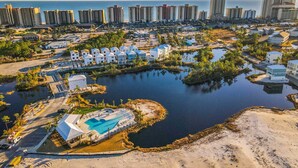 An aerial view of a coastal resort with a swimming pool, beachfront villas, and a marina. - Brand-new home near the beach with on-site pool, central AC, & washer,dryer (Orange Beach)