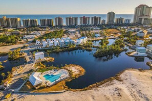 An aerial view of a coastal resort with a swimming pool, beachfront villas, and a marina. - Brand-new home near the beach with on-site pool, central AC, & washer,dryer (Orange Beach)
