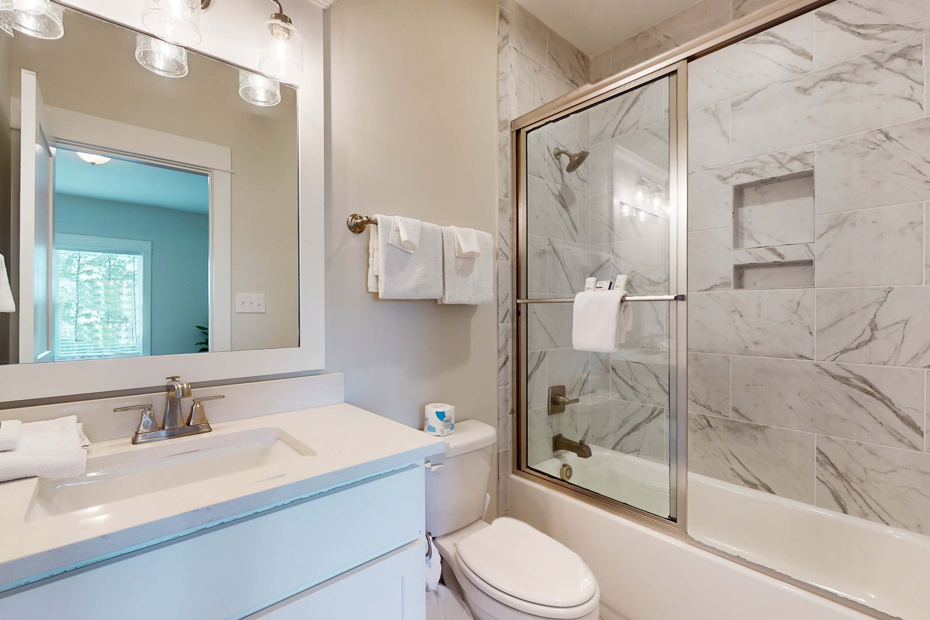A bathroom with a glass-enclosed shower, a white sink, and a mirror with lights.