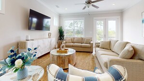 A living room with a sofa, armchairs, a coffee table, a TV, and a ceiling fan. - Brand-new home near the beach with on-site pool, central AC, & washer,dryer (Orange Beach)