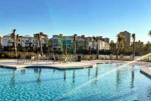 A swimming pool with lounge chairs and palm trees, surrounded by multi-story buildings. - Brand-new home near the beach with on-site pool, central AC, & washer,dryer (Orange Beach)