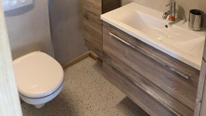 A bathroom with a toilet, a sink with a mirror, and a shower area. - Luxury Pipowagen, cottage in a private forest (Ravels)