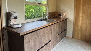 A kitchen with a wooden countertop, a sink, a window with a view of greenery, and a coffee maker. - Luxury Pipowagen, cottage in a private forest (Ravels)