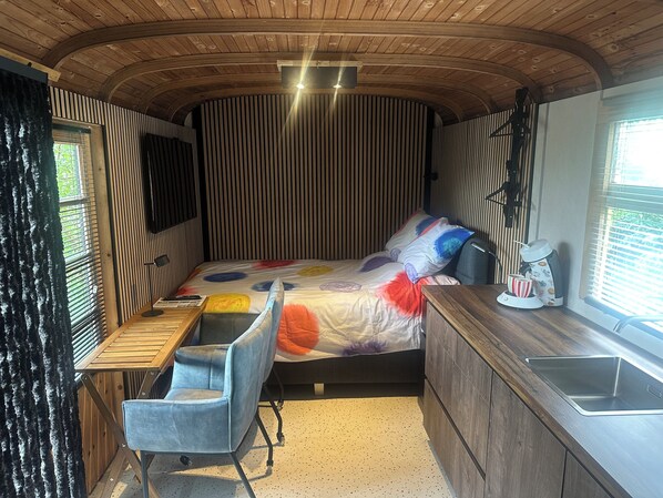 A compact bedroom with a bed, a desk, a chair, a window, and a sink.