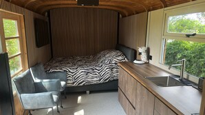A compact, modern room with a bed, a small desk, and a kitchenette. - Luxury Pipowagen, cottage in a private forest (Ravels)
