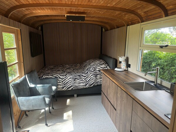 Une chambre compacte et moderne, équipée d’un lit, d’un petit bureau et d’une kitchenette.