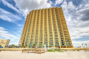A high-rise hotel with multiple balconies, a sandy beach in the foreground, and a clear sky. - Spacious condo with pool, hot tub, tennis courts, & sauna (Orange Beach)