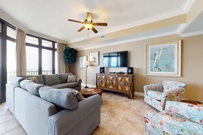 A living room with a sofa, armchairs, a coffee table, a TV, and a ceiling fan. - Spacious condo with pool, hot tub, tennis courts, & sauna (Orange Beach)