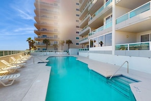 A rooftop pool with sun loungers, a clear sky, and a high-rise building in the background. - Top-floor, dog-friendly condo right on the beach with pool & fantastic views (Orange Beach)