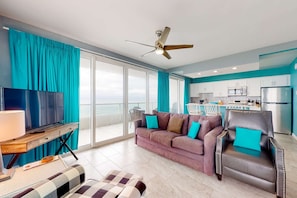 A modern living room with a sofa, armchair, TV, and a ceiling fan. - Top-floor, dog-friendly condo right on the beach with pool & fantastic views (Orange Beach)