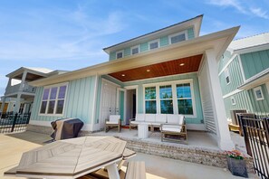 A two-story house with a covered patio, outdoor seating, and a large window overlooking the yard. - Modern beach house with porches, private washer and dryer- walk to the beach (Orange Beach)
