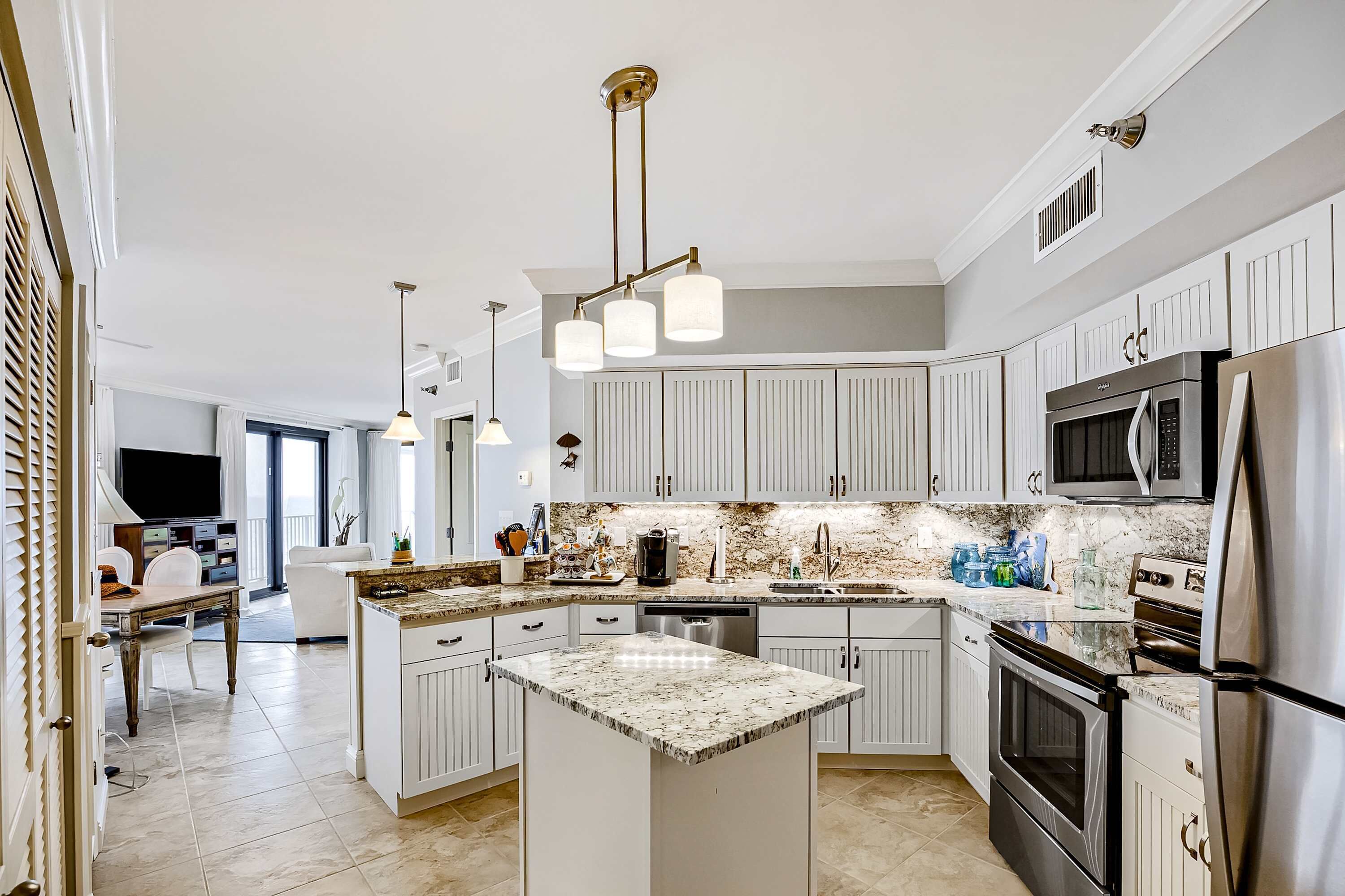 A modern kitchen with white cabinetry, a central island, stainless steel appliances, and pendant lighting.