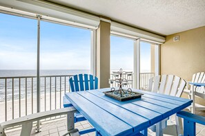 Un balcon avec vue sur l’océan, une table bleue avec des chaises et un petit objet décoratif posé sur la table.