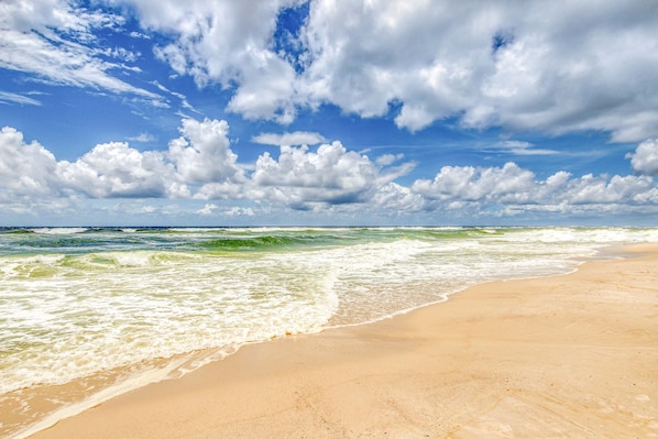 Een strand met golven, een heldere lucht en wolken.