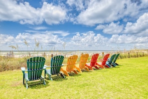 Een rij kleurrijke Adirondack-stoelen staan op een gazon met uitzicht op het strand en de oceaan.