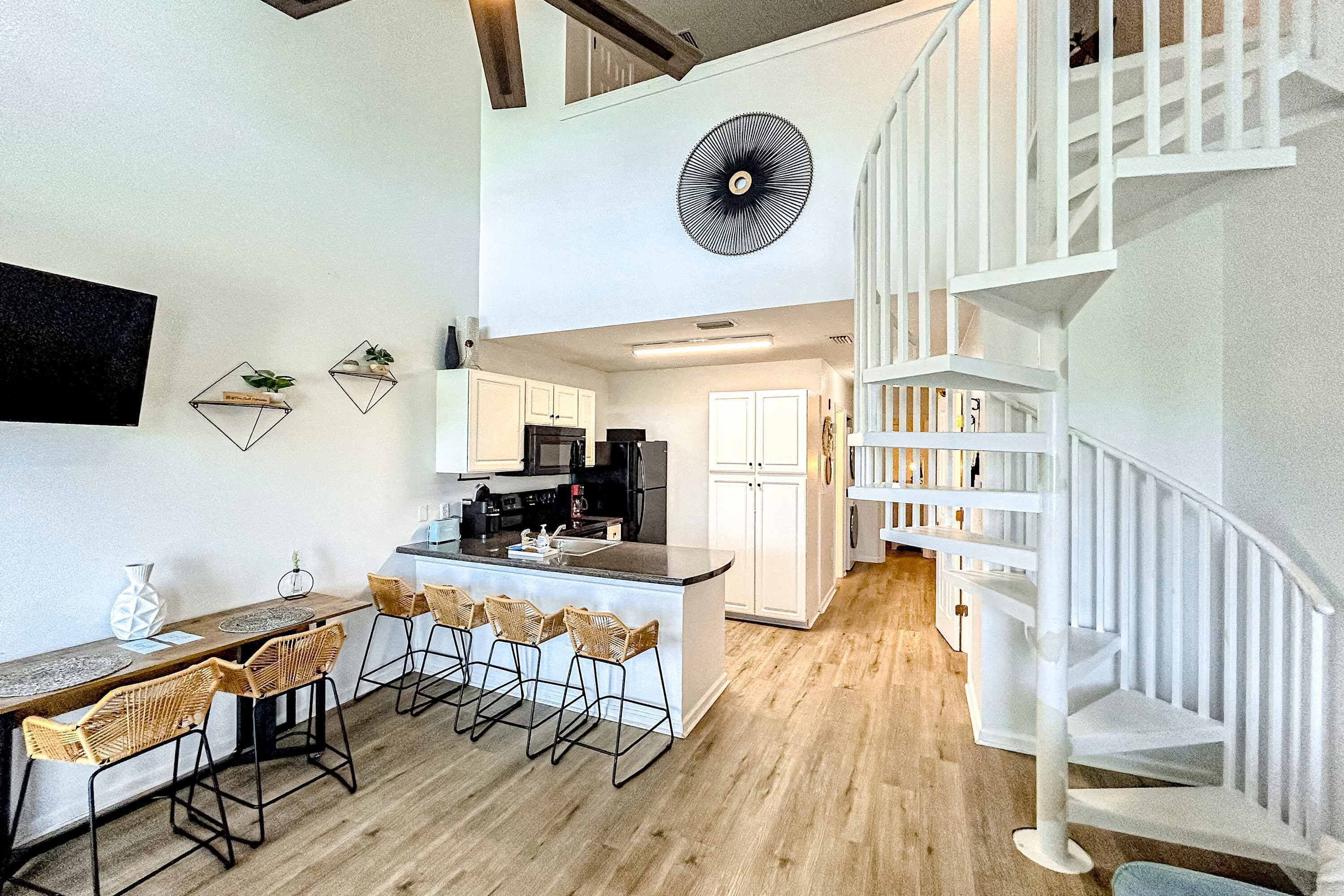 A modern kitchen with white cabinets, a central island with bar stools, and a white staircase.