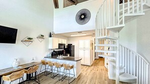 Una cocina moderna con armarios blancos, una isla central con taburetes de bar y una escalera blanca.