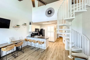 Eine moderne Küche mit weißen Schränken, einer zentralen Kochinsel mit Barhocker und einer weißen Treppe.