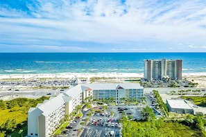 Ein Hotel mit Parkplatz, Blick auf den Strand und einem hohen Gebäude im Hintergrund.