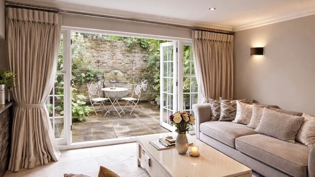 A living room with a sofa, a coffee table, and a view of an outdoor patio with a brick wall and greenery.