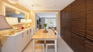 A modern dining area with a wooden table, white chairs, a large mirror, and a dark wooden cabinet.