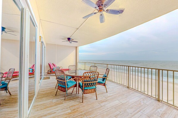 Een balkon met rieten meubilair, een plafondventilator en uitzicht op zee.