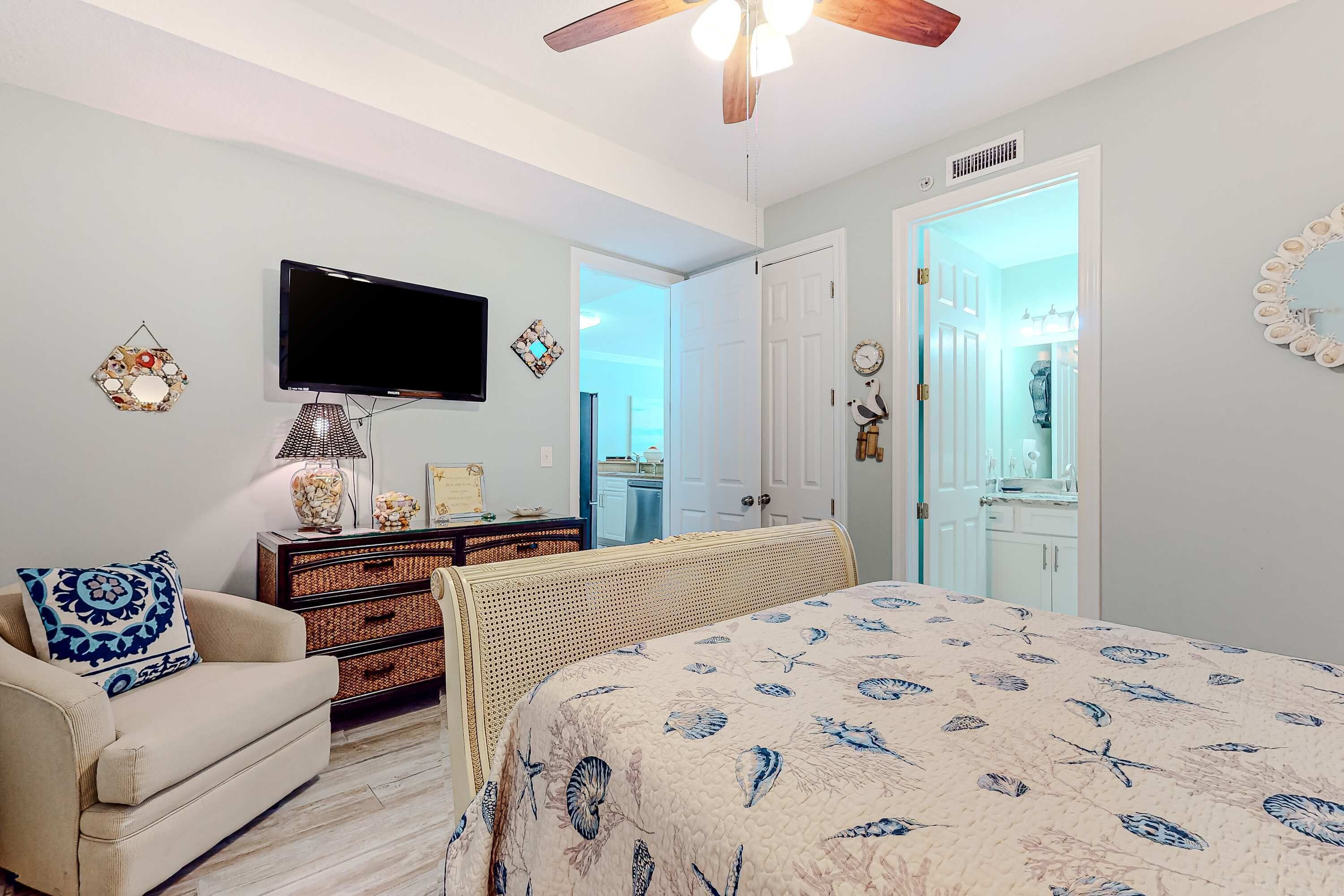 Un dormitorio con una cama, televisión, cómoda, silla y puerta que da a otra habitación.