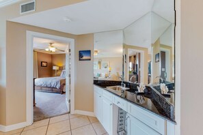 Habitación de hotel con un espejo grande, una cama, un baño con lavamanos y un pasillo que conduce a otra habitación.
