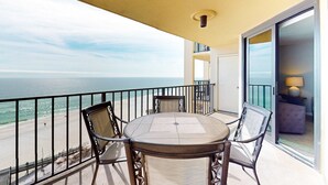A balcony with a table and chairs, a view of the ocean, and a sliding glass door leading to an interior space. - Renovated beachfront condo with balcony, central AC, pool, hot tub & tennis (Orange Beach)