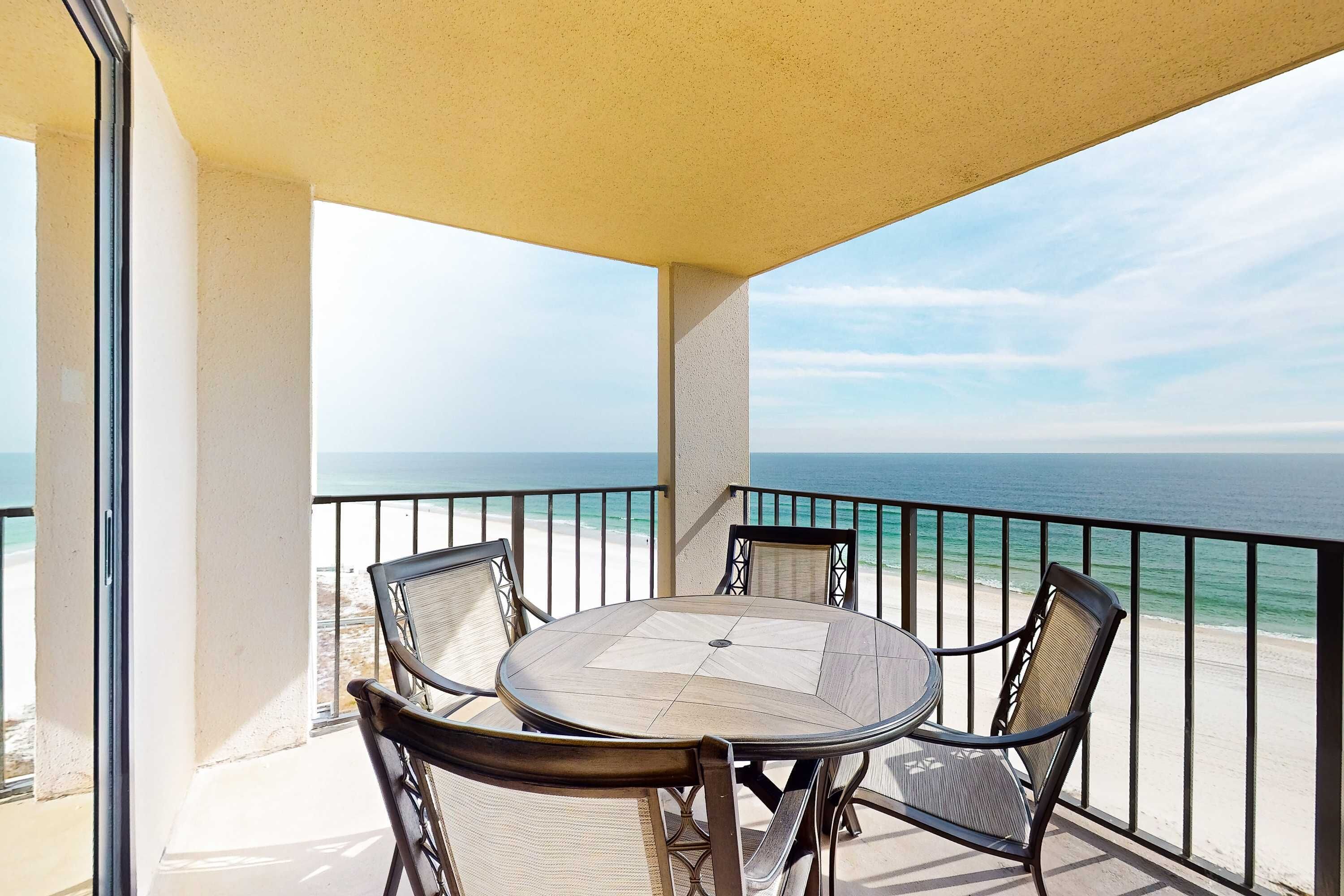 Un balcon avec une table ronde et des chaises, donnant sur une plage et l’océan.