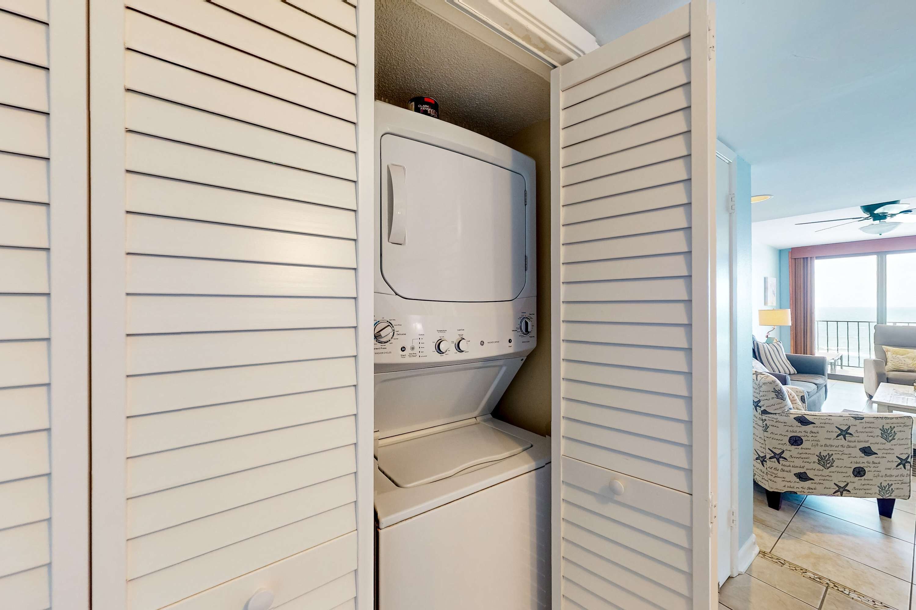 Ein Waschraum mit einer Waschmaschine und einem Trockner, einem Deckenventilator und Blick auf einen Wohnbereich mit Sofa und Lampe.