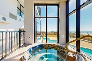 A hot tub with a view of a beach and pool, large windows, and a balcony railing. - Phoenix II condo with Gulf views, shared pool, hot tub, sauna, tennis, & WiFi (Orange Beach)