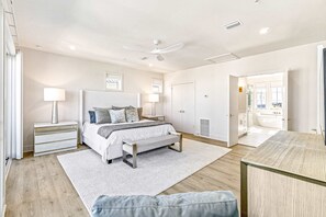 A bedroom with a bed, bedside tables, a bench, a ceiling fan, and a view into the bathroom. - Spacious beachside community home with ocean view, private pool, & fireplace (Orange Beach)