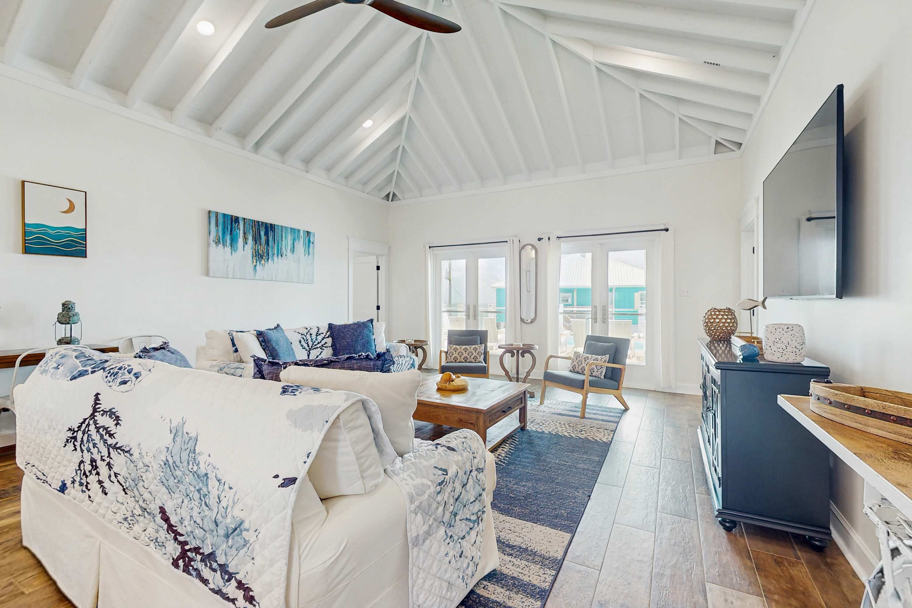 A spacious living room with a high ceiling, a large window, a sofa set, a coffee table, and a TV mounted on the wall.