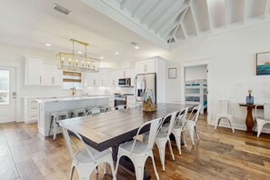 A spacious kitchen with white cabinetry, a central island, and a large dining table with chairs. - Gulf-Front Oasis: Rooftop Heated Pool, Elevator & Dog-Friendly! (Dauphin Island)