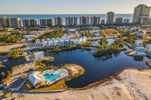 An aerial view of a coastal resort with a large swimming pool, beachfront villas, and a marina. - Upscale beachside dog-friendly home near the beach with grill, washer,dryer & AC (Orange Beach)