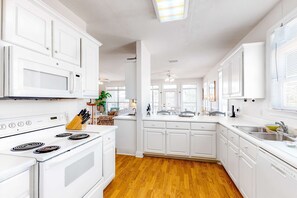 A kitchen with white cabinets, a microwave, stove, and a sink. - Bright duplex with two full kitchens, large decks, and private washer/dryers (Dauphin Island)