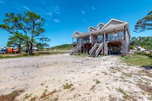 Ein zweistöckiges Strandhaus mit Balkon und Treppe, vor der Tür ein Sandstrand.