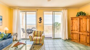 A living room with a sofa, a striped armchair, a glass coffee table, a wooden cabinet, and a view of the balcony. - Gulf-front condo w/ lock-out feature, shared pools & amazing views (Dauphin Island)