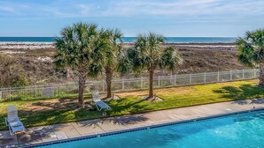 A pool with a view of the beach, palm trees, and a fenced area with lounge chairs. - Gulf-front condo w/ lock-out feature, shared pools & amazing views (Dauphin Island)
