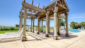 Una estructura de pérgola de madera con una piscina y sillones de descanso al fondo.