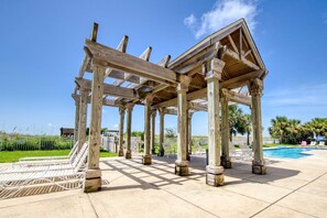 A wooden pergola structure with a pool and lounge chairs in the background. - Ground-floor condo with beachfront access, pool, patio, & 2 full kitchens (Dauphin Island)