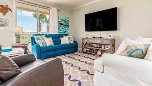 Una sala de estar con un sofá azul, un sofá blanco, un televisor de pantalla plana y una alfombra estampada.